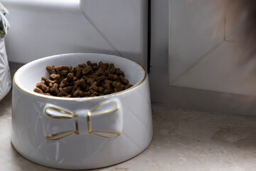 Pet food bowl designed with a bow holds kibble near a sunny window on a calm morning