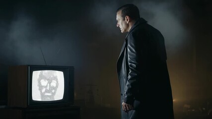 Reacting to screen flickering, man in coat watching glitching TV face in smoky room, copy space - Powered by Adobe