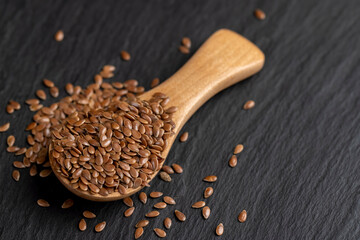 flax seeds poured into a wooden spoon on black slate , glossy black surface with a wooden spoon filled with flax seeds