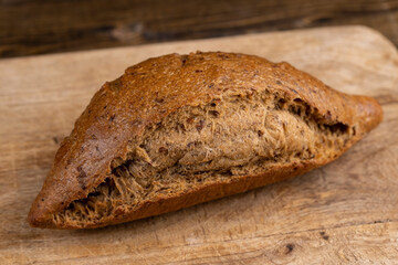 a whole small loaf of rye flour bread lies on the table on a cutting board, a small elongated loaf of freshly baked rye bread on an old cutting board for slicing bread