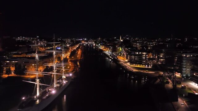 Aerial view flying along the Aura river, night in illuminated Turku city, Finland
