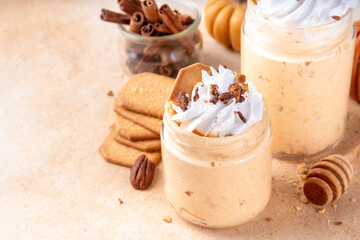 Pumpkin pie overnight oatmeal with whipped cream, nuts and graham crackers. Tasty creamy pumpkin spice oats, on beige background with spice and decorative pumpkins, copy space