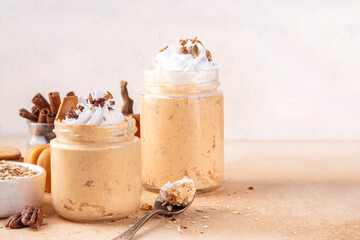 Pumpkin pie overnight oatmeal with whipped cream, nuts and graham crackers. Tasty creamy pumpkin spice oats, on beige background with spice and decorative pumpkins, copy space