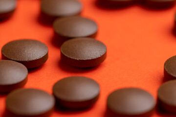 brown tablets lying on orange paper without packaging, a large number of brown tablets as medicine on an orange paper surface