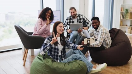 Group of diverse young adults sitting on beanbags in bright modern office posing for selfie. Relaxed and cheerful atmosphere. Ideal for concepts of teamwork, friendship, and modern workplace dynamics. - Powered by Adobe