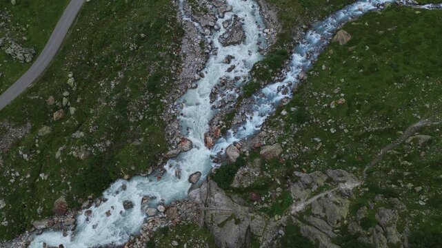 Wld river with glacial meltwater flowing over rocks, Swiss Alps. Aerial top-down descending