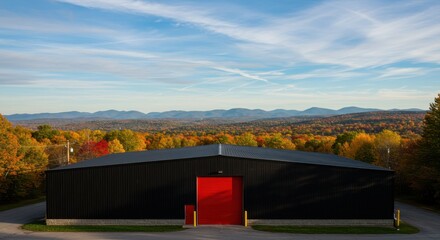 Obraz premium Modern Black Warehouse Structure Against Stunning Autumn Landscape with Colorful Foliage and Distant Mountains
