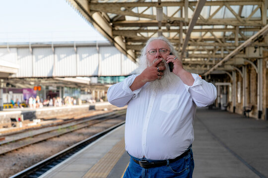 Mature man picks his nose while talking on his cell phone at a train station on a sunny day