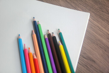 Close-up of a fan of vibrant colored pencils arranged on a plain white sheet of paper on a wooden desk.
