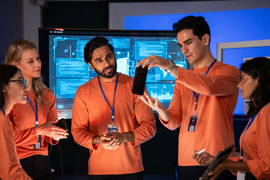 Diverse team of professionals collaborating on a project presentation using a smartphone, Startup colleagues discussing mobile app design and development, brainstorming ideas in the office