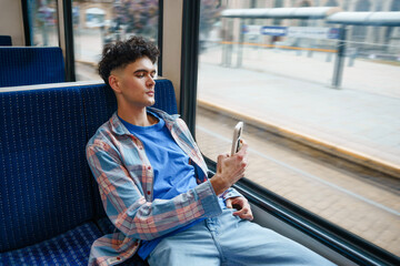 Young man looking at phone on a tram traveling through City
