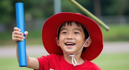 An elementary school student wearing a gym uniform and cap smiles while holding the baton after winning a race.