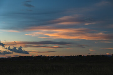 ambiente di campagna tra pianura e collina al tramonto, con cielo leggermente nuvoloso, con nuvole rosa ed arancioni