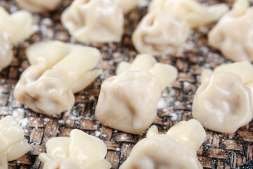 Handmade wontons with flour on wooden board ready for cooking in clear broth