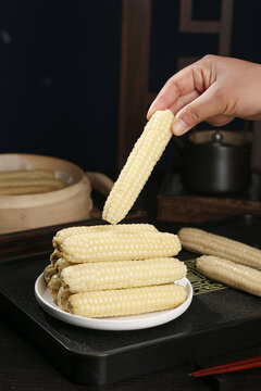 Hand Holding Fresh Mini White Corn Cob in Traditional Kitchen Setting