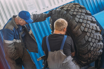 Two mechanics are working together to repair a large tire in a workshop. The environment is industrial and focused on teamwork and maintenance.