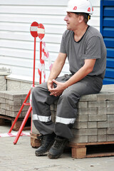 Caucasian male construction worker in hard hat sitting on concrete blocks.