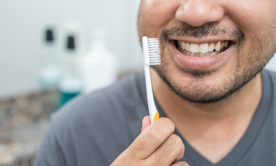 Man with toothbrush cleaning teeth and looking to mirror at bathroom. Oral hygiene routine for freshness breath prevent plaque gum disease. Dental health care Oral hygiene and teeth care concept.