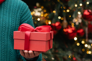 Man hand holding red gift box or present against Christmas tree. Xmas shopping. Close up. Greeting card. Boxing Day.