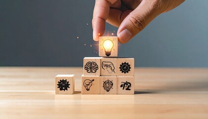 Wooden blocks stacked, forming a pyramid, with icons depicting ideas. A hand places a block with a lightbulb icon on top