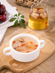 Sweet Chinese dessert soup with longan dates and goji berries served in white ceramic bowl on wooden board