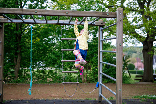 Little girl doing gymnastics on a climbing frame, horizontal bar on school yard. Child enjoying school break.