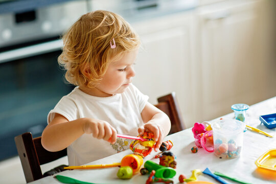 Adorable cute little toddler girl with colorful clay at home. Healthy baby playing and creating toys from play dough at nursery or playschool. Small kid molding modeling clay, creative activity