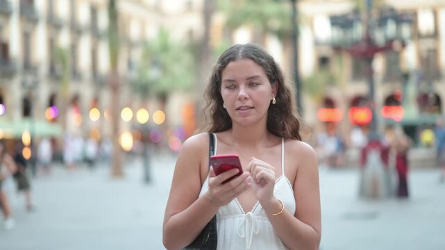 Young woman in summer clothes and with a phone in hands walks through the streets of Barcelona, she wants to meet friends and go to a restaurant in the evening
