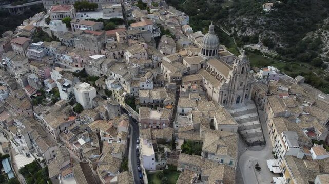 Aerial drone footage of Ragusa in Sicily during the day with clouds, focusing on Duomo di San Giorgio and the historic city center while also showing the wider town and its unique architecture.