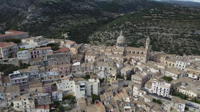 Aerial drone footage of Ragusa in Sicily during the day with clouds, focusing on Duomo di San Giorgio and the historic city center while also showing the wider town and its unique architecture.