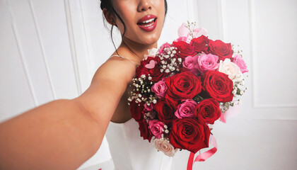 happy woman takes a selfie while holding a vibrant bouquet of red and pink roses on white background.