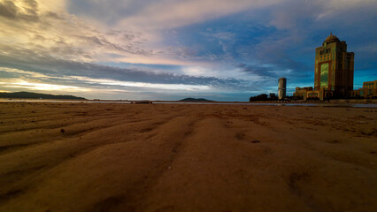 Kota Kinabalu, Sabah, Malaysia – a beach panorama at low tide at sunset. The sunset sky, reflections on the sand, and modern buildings on the coast of Borneo. A popular travel destination in Southeast
