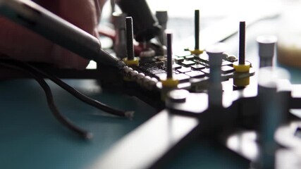 A specialist performs soldering on an FPV drone, attaching power and signal wires to its control board. - Powered by Adobe