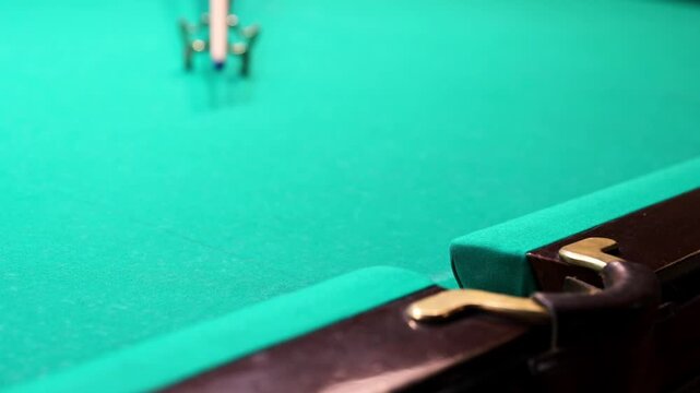 Close-up of a white billiard ball being hit with a cue and falling into the corner pocket of a green table