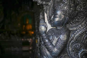 Ornate silver toned statue with hands pressed together devout prayer gesture. Intricately detailed carving depicts serene spiritual figure, radiating peace within traditional temple setting