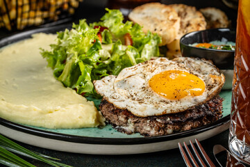 Beef patty with fried egg, mashed potatoes and salad