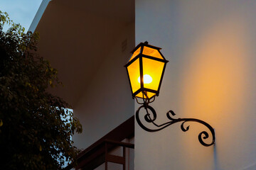 Yellow wall-mounted lantern glows against a white building facade at twilight.
