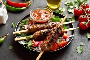 Prepared lula kebab on skewers served with fresh vegetables and sauce
