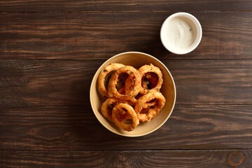 Crispy fried onion rings in bowl on wooden table