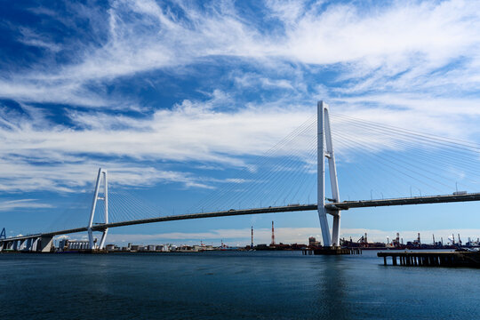 The Meiko Chuo Bridge, a white cable-stayed bridge spanning Nagoya Port in Aichi Prefecture, Japan. The bright blue sky and calm sea emphasize the elegant engineering structure.
