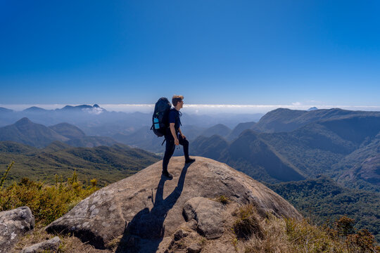 A hiker with a backpack on the mountaintop along the long-distance trail between the cities of Petr&oacute;polis and Teres&oacute;polis, in the mountainous region of Rio de Janeiro, enjoying a beautiful panoramic v