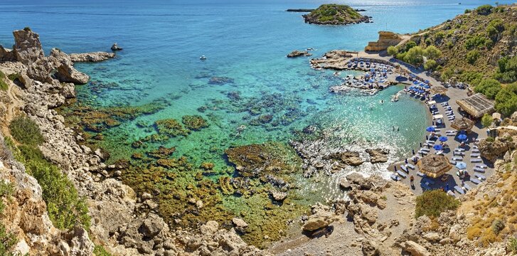Secluded Grande Blue Bay with clear turquoise water and rocks, along which a row of beach loungers and parasols stretches, Grande Blue Beach, Stegna, Archangelos, Rhodes Island, Greece