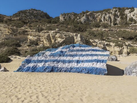 Rock painted with a Greek flag on the sandy Tsambika beach under a clear sky, Tsambika beach, Archaggelos, Rhodes island, Greece