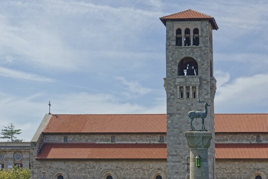 A church Ekklisia Evaggelismos with red roof and bell tower, in the foreground the deer cow statue (Colossus of Rhodes), Mandraki harbour, Medieval town of Rhodes, Rhodes island, Greece