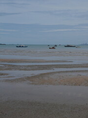low tide sandy beach with shallow water pools and fishing boats on calm horizon