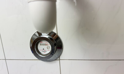 Water meter installed on bathroom pipe under sink with chrome cover showing measurement dial for...