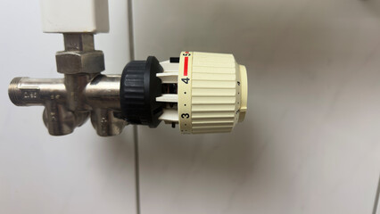 Radiator thermostat valve close up with temperature control knob on heating system pipe indoors for regulating room heat energy in modern apartment or house
