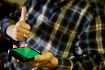 Man holding smartphone with thumbs up gesture indoors