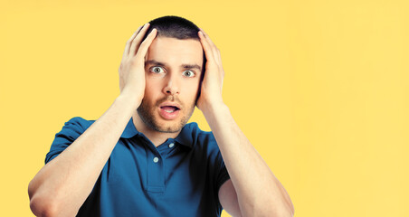 Portrait of shock or surprised man with wide open eyes, mouth, hold hands on head, isolated against yellow background. Face emotion, thinking, business idea concept ad image.