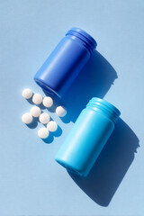 Two Pill Bottles Lying on Their Sides – One with White Pills, One with Blue Pills.